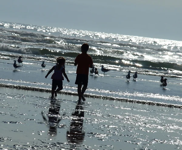 Двое детей играют на пляже, как солнце светит на воде — стоковое фото