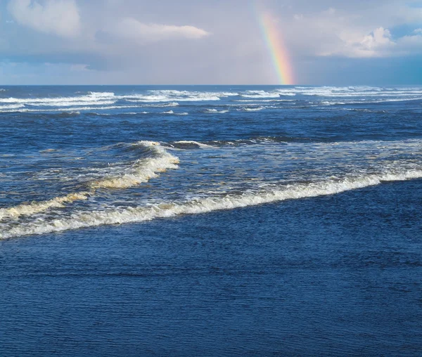 Ondas do oceano quebrando na costa com um arco-íris parcial no fundo — Fotografia de Stock