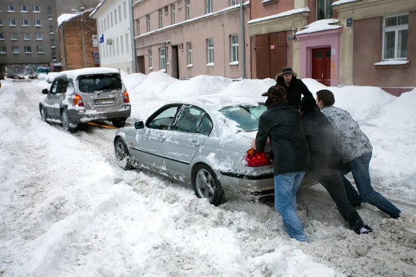Empujando atrapado coche en la calle Nevada después de fuertes nevadas en riga —  Fotos de Stock