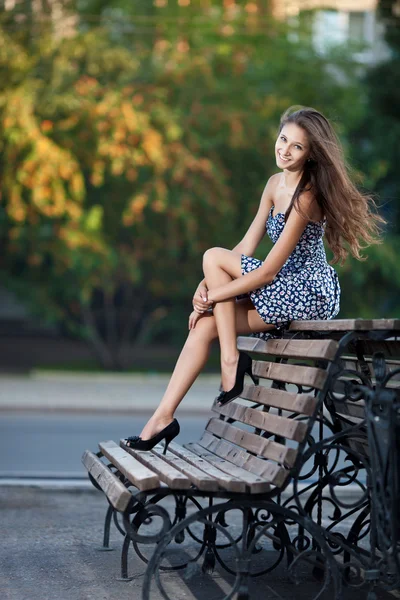 Wspaniała brunetka siedzi na ławce, który znajduje się na ulicy miasta — Zdjęcie stockowe
