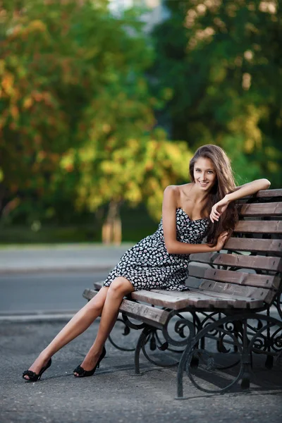 Wspaniała brunetka siedzi na ławce, który znajduje się na ulicy miasta — Zdjęcie stockowe
