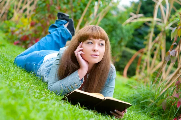 Молода жінка читає книгу, що лежить на траві — стокове фото