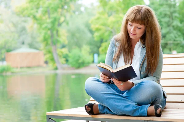 Молодая женщина читает книгу, сидя на скамейке — стоковое фото