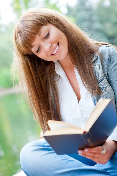 Jovem mulher lendo um livro sentado no banco — Fotografia de Stock