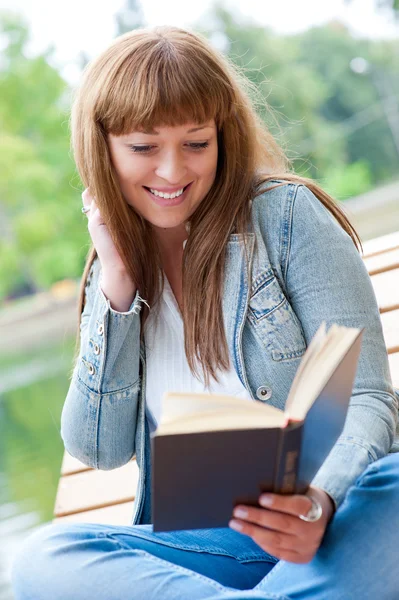 Genç kadın bankta oturan bir kitap okuma — Stok fotoğraf