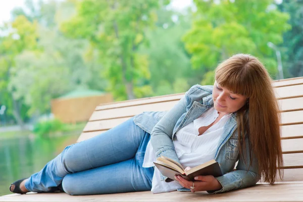 Jovem mulher lendo um livro sentado no banco — Fotografia de Stock