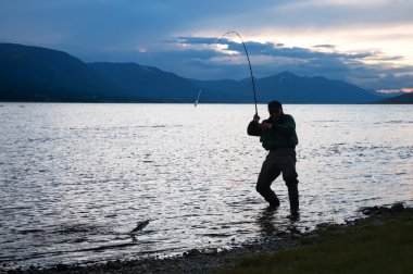 Silhouette of a fisherman pulling a fish clipart