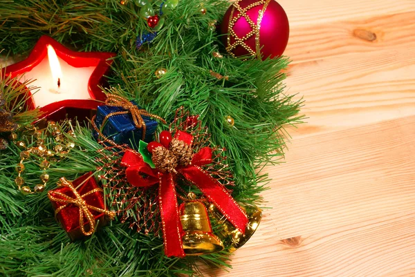 Trevlig xmas dekorationer: röd sfär, gyllene klockor med rött band, rött ljus och grön jul krans över trä skrivbord — Stockfoto