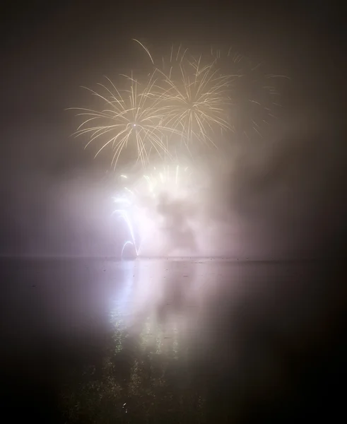 Kleurrijke vuurwerk op de achtergrond van de zwarte lucht en het water weerspiegelen — Stockfoto