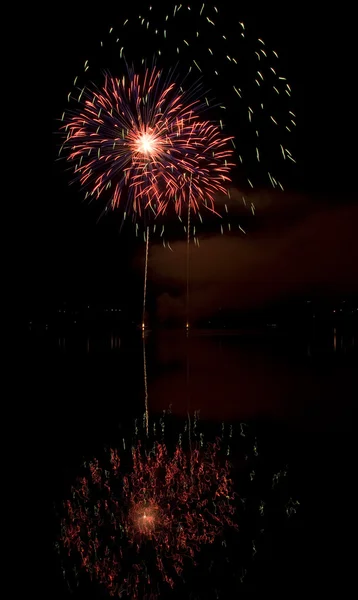 Fuochi d'artificio colorati su sfondo cielo nero con riflesso acqua — Foto Stock