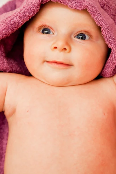 Säuglingsbaby lächelnd in violettem Handtuch liegend — Stockfoto