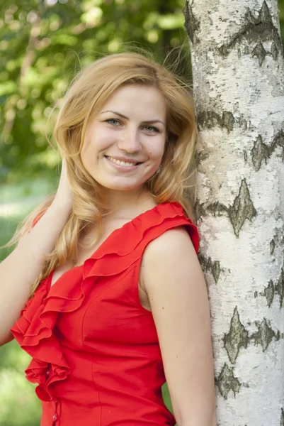 Gülümsüyor ve bir huş ağacı kucaklayan kırmızı bir bluz kız portresi. — Stok fotoğraf