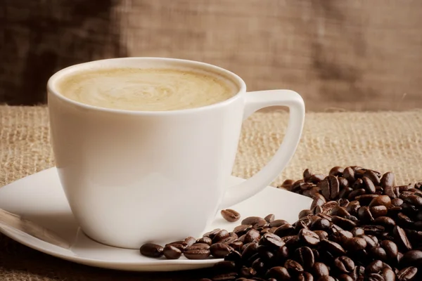 Cappuccino och kaffebönor över säckväv — Stockfoto