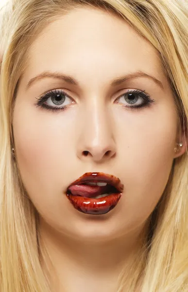 Beautiful blonde woman licking chocolate from her chocolate covered lips — Stock Photo, Image