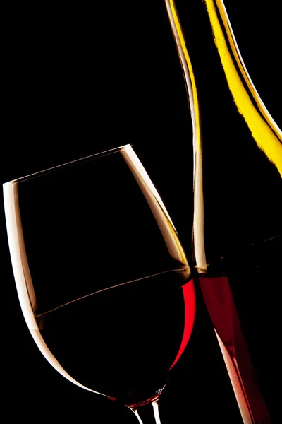 Backlit detail of a glass of red wine and the wine bottle — Stock Photo, Image