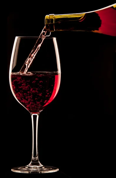 Gieten van een glas rode wijn op zwarte achtergrond. — Stockfoto