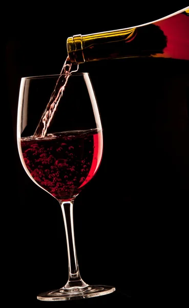 Ein Glas Rotwein auf schwarzem Hintergrund gießen. — Stockfoto