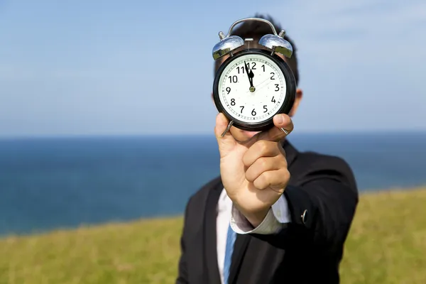 Stock image Businessman holding clock and standing on the field