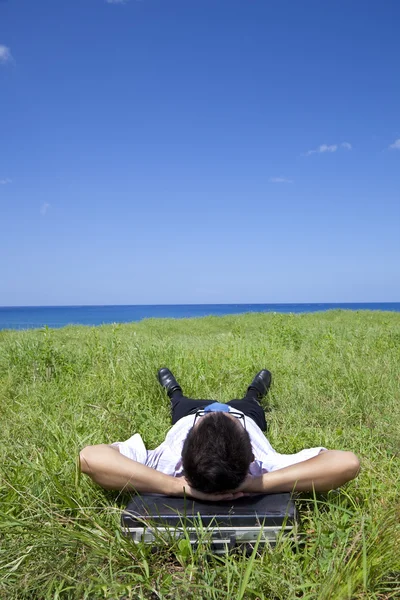 Uomo d'affari sdraiato sull'erba verde e guardando il cielo blu — Foto Stock