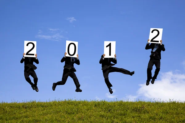 Empresario sosteniendo la cartelera 2012 y saltando en el campo verde — Foto de Stock