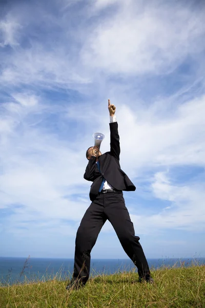 Бизнесмен стоит на холме и держит мегафон с облачным фоном — стоковое фото