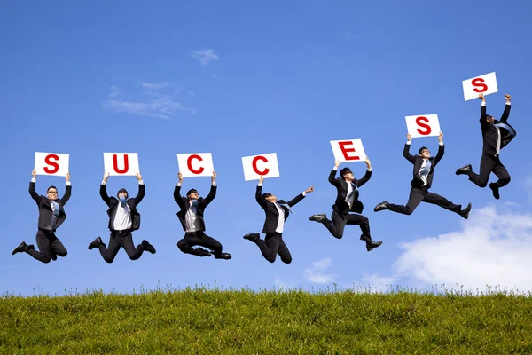 Homem de negócios feliz segurando texto de sucesso e pulando no campo verde — Fotografia de Stock