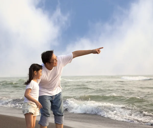 Отец указывает и маленькая девочка смотрит на него на пляже — стоковое фото