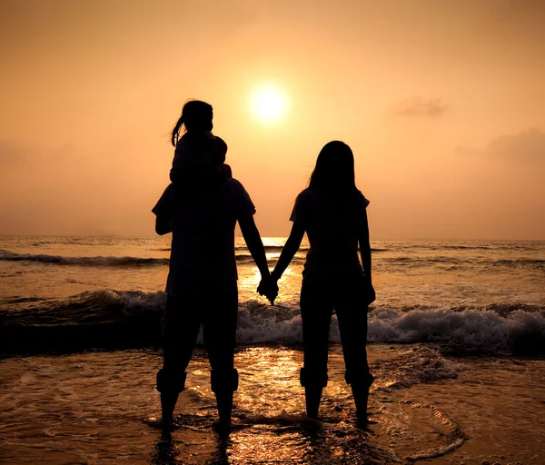 Силуэт любящей азиатской семьи, идущей, держась за руки на пляже — стоковое фото