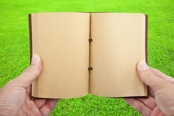 Opened book in hand on the grass field — Stock Photo, Image