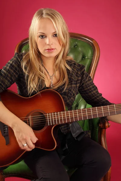 Kobieta gitarzysta siedzi na skórzanym fotelu — Zdjęcie stockowe