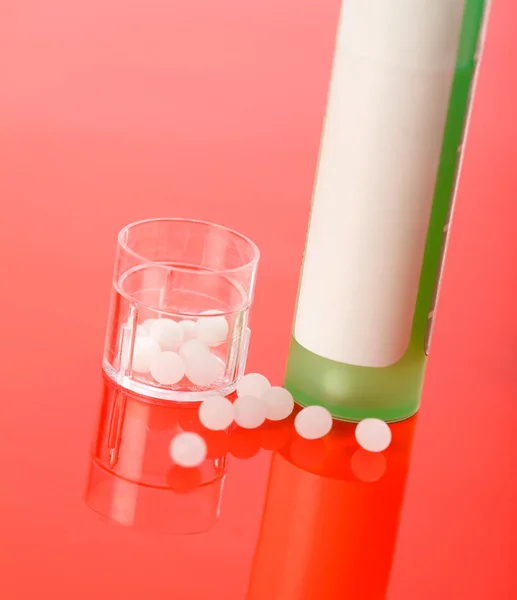 Comprimidos homeopáticos e recipiente em vermelho — Fotografia de Stock