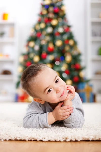 Милый мальчик, лежащий перед рождественской елкой — стоковое фото
