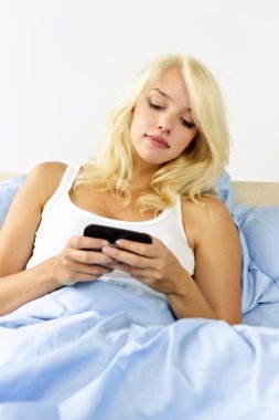 Woman in bed with cell phone texting clipart