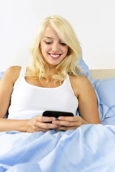 テキスト メッセージのベッドに座っている女性 — ストック写真