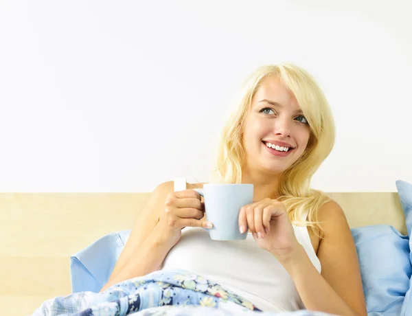 Genç bir kadın kahve fincanıyla yatakta. — Stok fotoğraf