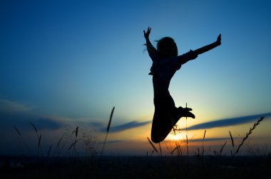 Silhouette of a girl jumping over sunset clipart