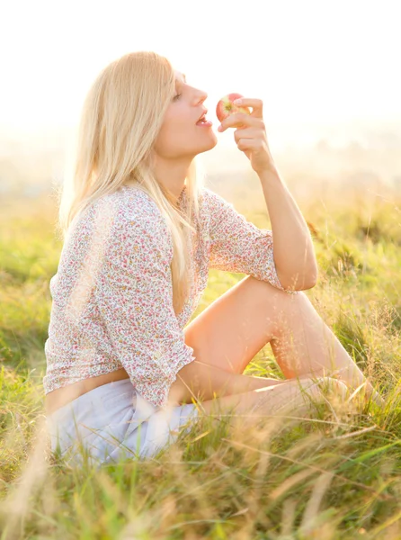Girl is eating apple sitting on green field — Stock Photo, Image