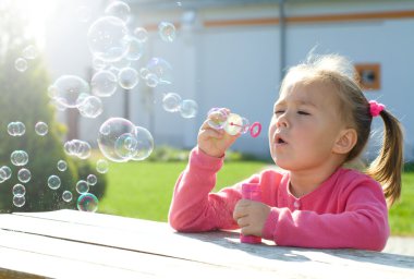 Little girl is blowing soap bubbles clipart