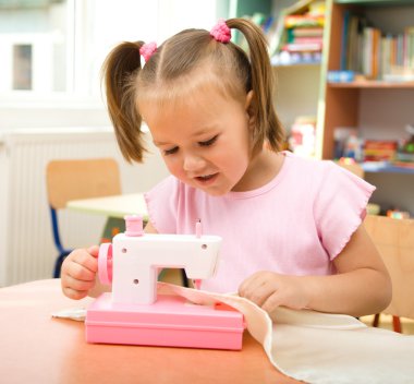 Little girl is playing with sewing machine clipart