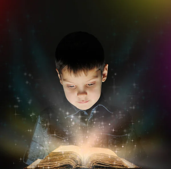O rapaz está a ler um livro mágico. — Fotografia de Stock