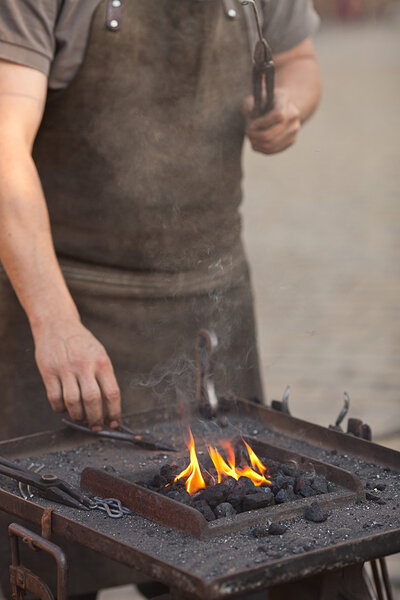 Embers, fire, smoke, tools and the hands of a blacksmith
