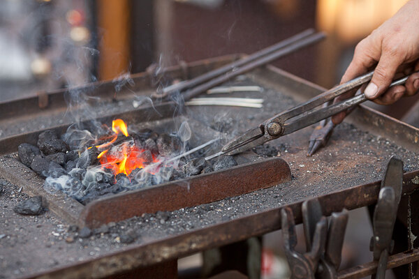 Embers, fire, smoke, tools and the hands of a blacksmith