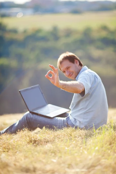 Jonge man met behulp van laptop zittend op het gras op de heuvel — Stockfoto