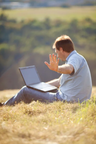 Hillside çimlere oturup dizüstü kullanan genç adam — Stok fotoğraf