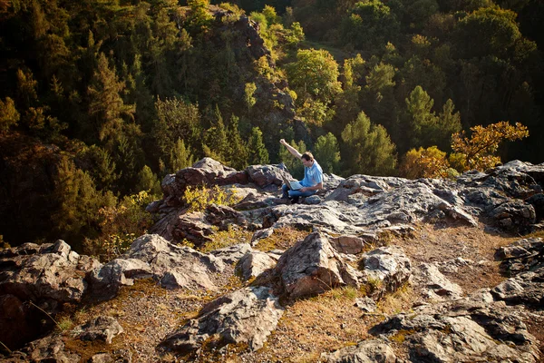 Молодой человек с ноутбуком, сидящий на скальном склоне — стоковое фото