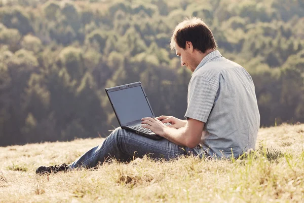 Hillside çimlere oturup dizüstü kullanan genç adam — Stok fotoğraf