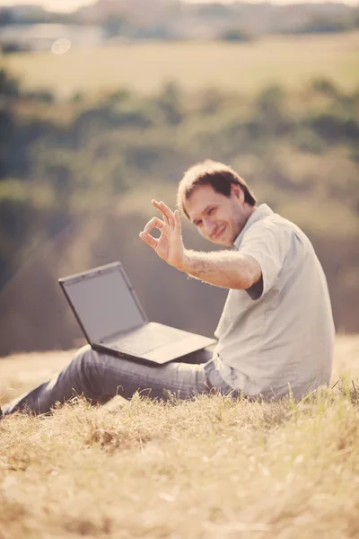 Young man using laptop sitting on the grass on the hillside — Stock Photo, Image