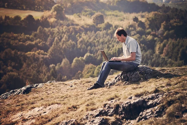 Fiatal ember használ laptop ül a fűben, a hegyoldalban — Stock Fotó