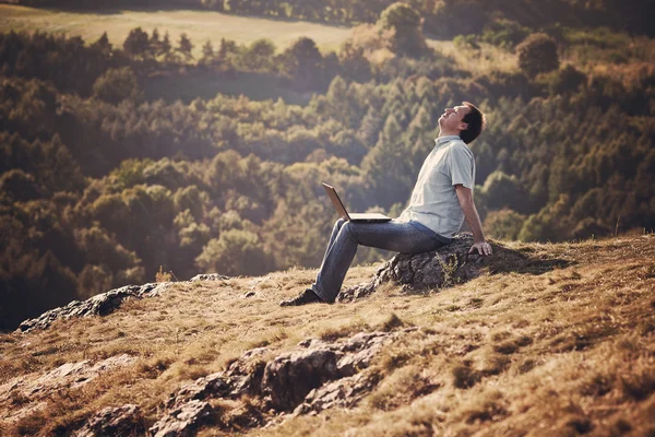 Jeune homme utilisant un ordinateur portable assis sur l'herbe sur la colline — Photo