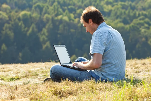 Jonge man met behulp van laptop zittend op het gras op de heuvel Stockfoto
